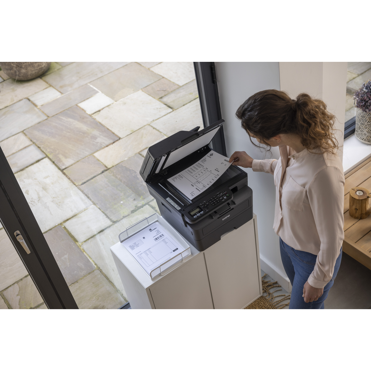 Woman scanning a document with a black printer. A white cabinet and stone patio are visible in the background.