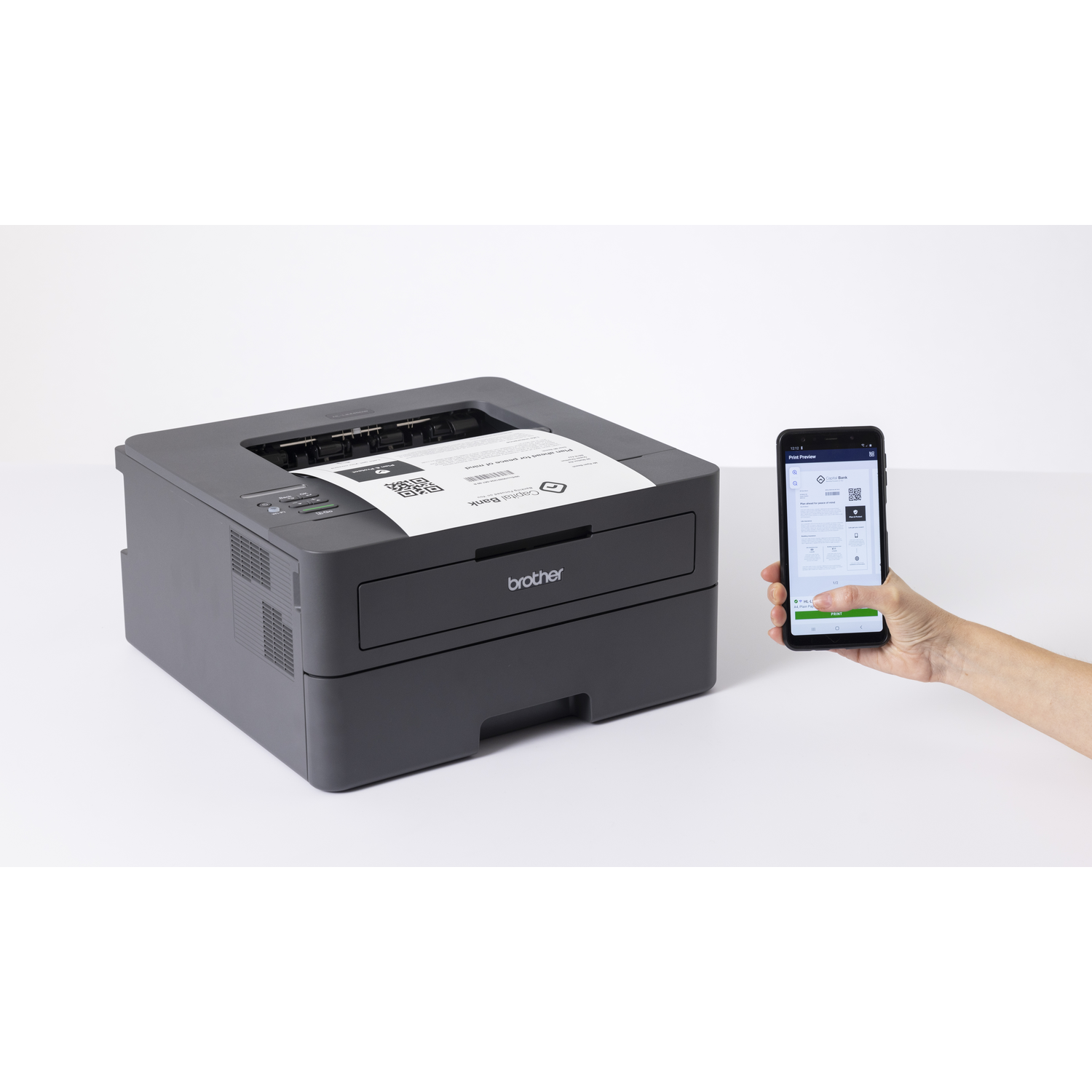 Een grijze Brother-printer die een document afdrukt. Een hand houdt een telefoon vast met een afdrukvoorbeeld. Witte achtergrond.