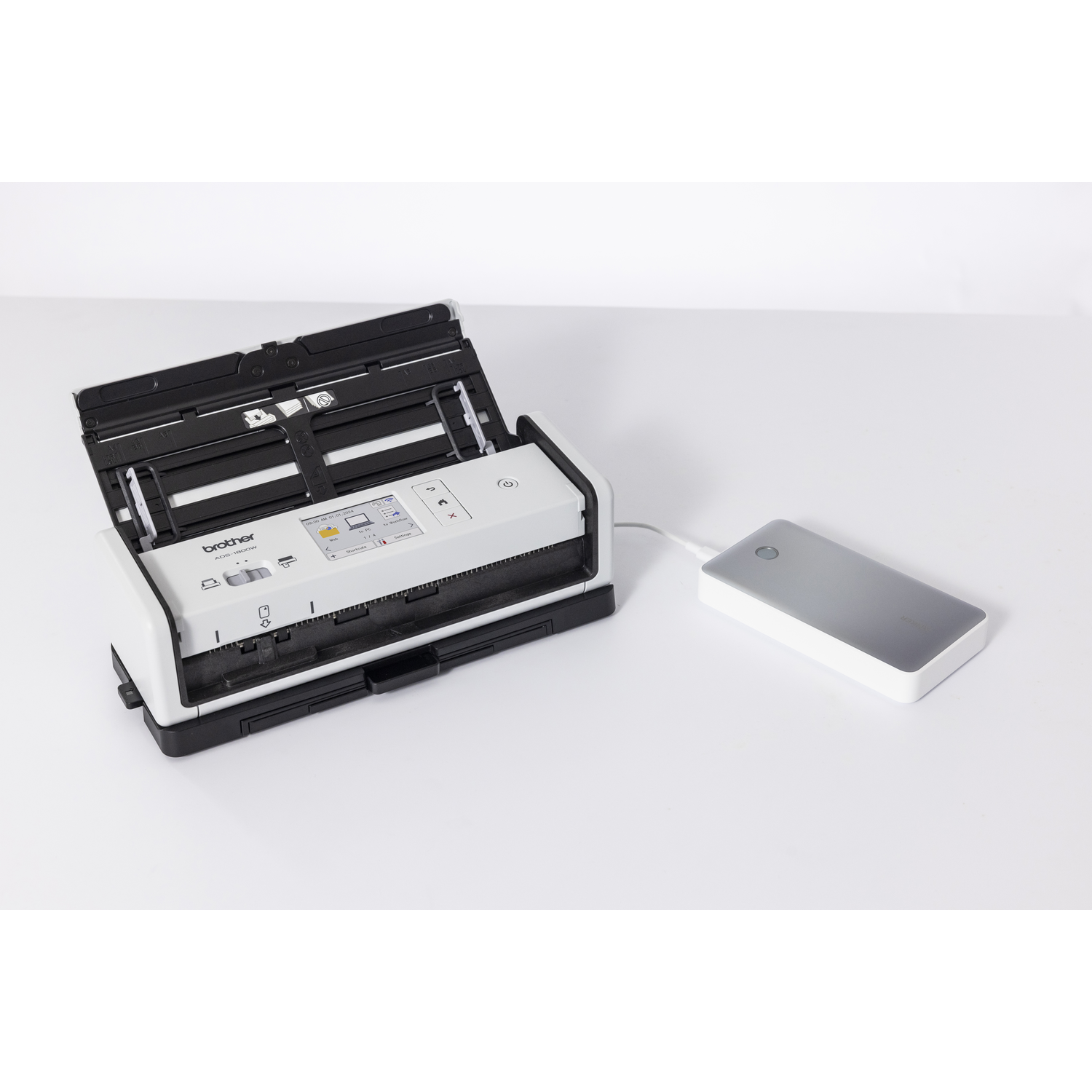 Een witte Brother-scanner met open deksel en een grijze externe harde schijf op een wit oppervlak.