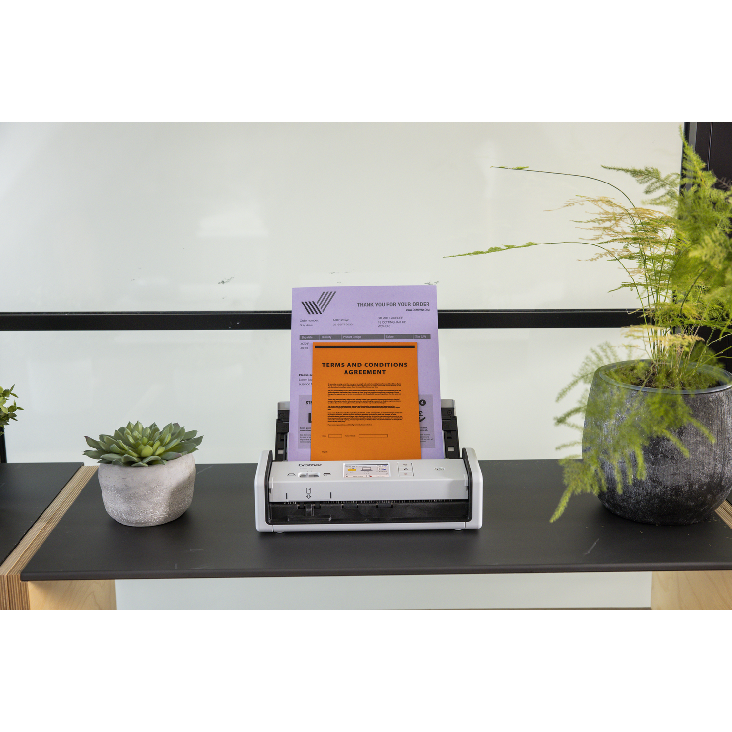 Een scanner met papieren. Links een vetplant in een pot en rechts een plant in een donkere pot.