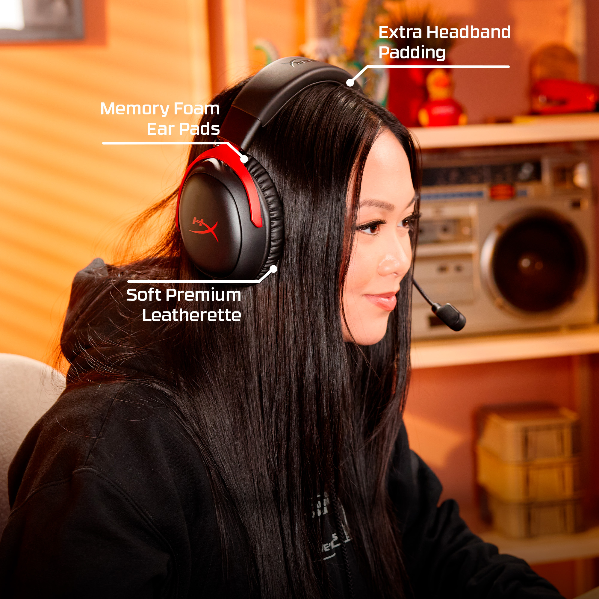 Eine Frau mit schwarzem Headset, schwarzem Hoodie und langen schwarzen Haaren. Im Hintergrund befinden sich eine Boombox und Regale.
