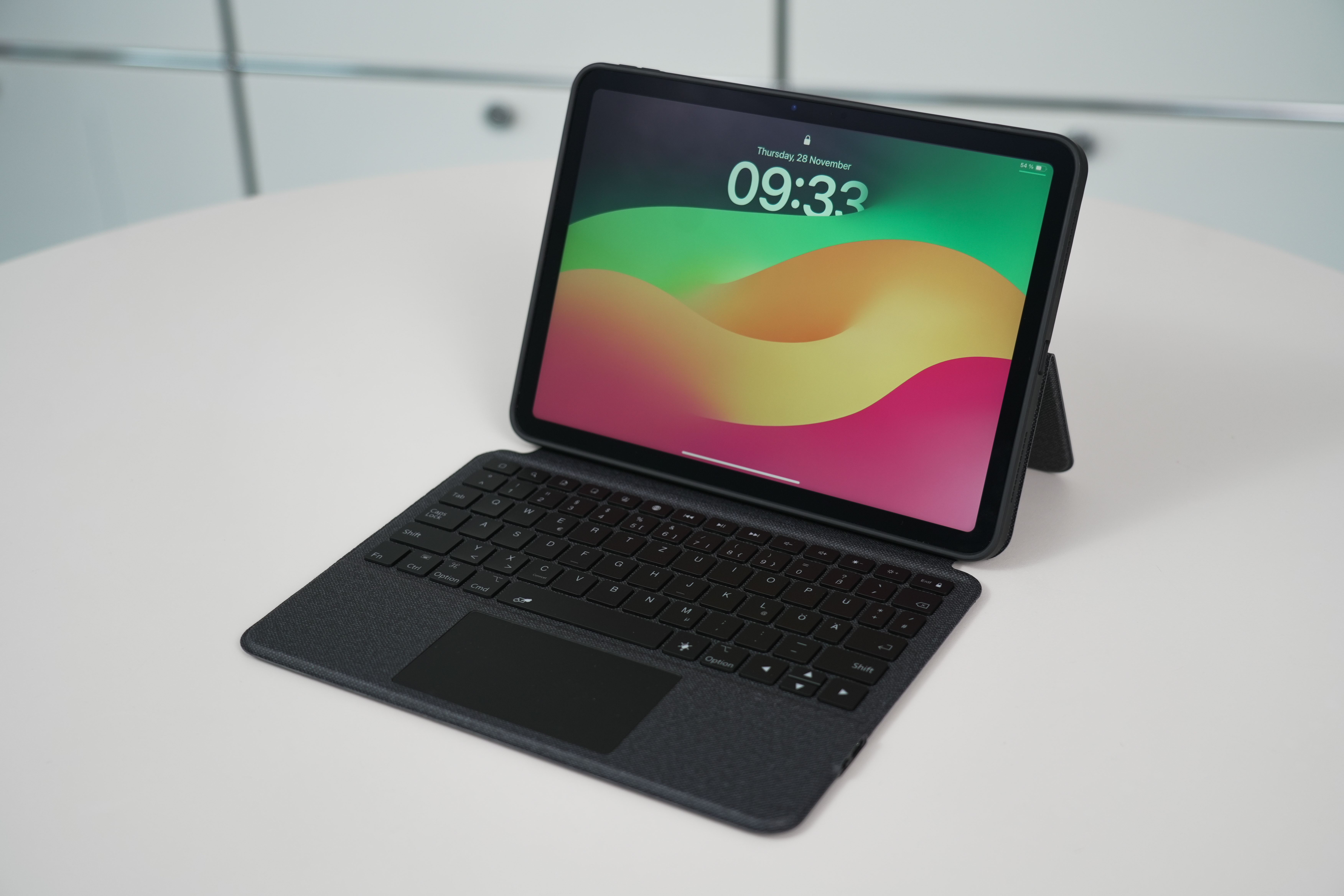 Tablet mit Tastatur auf weißer Oberfläche. Der Bildschirm zeigt die Uhrzeit. Tastaturtasten sind schwarz.