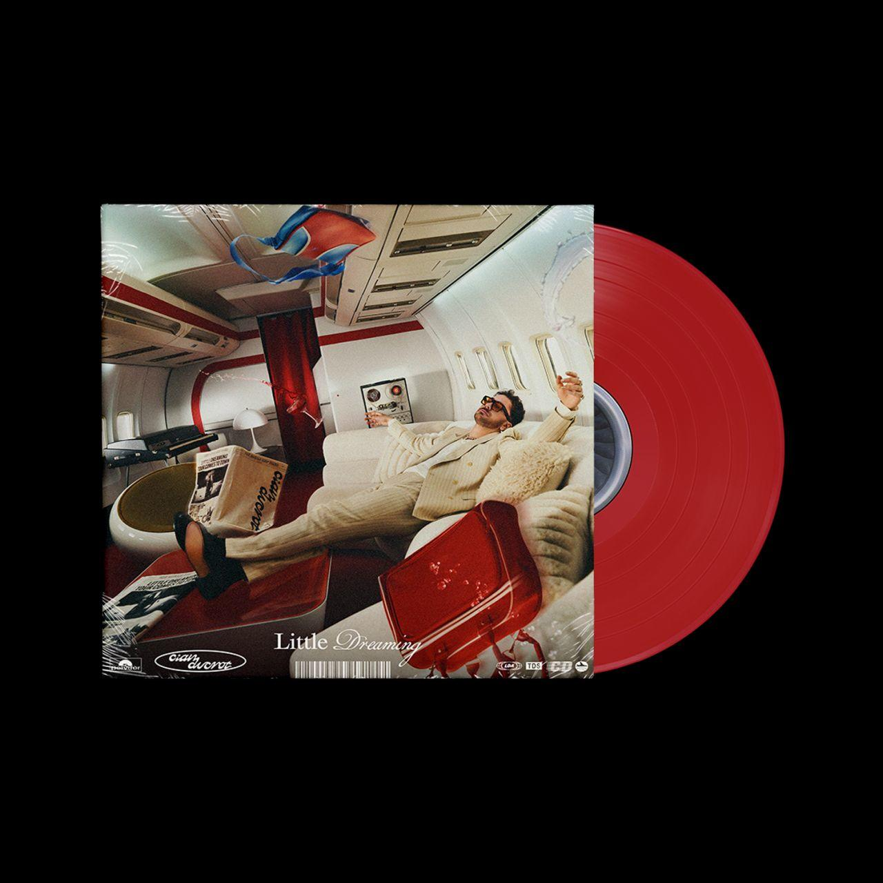 Mann im Anzug entspannt sich auf einem Flugzeugsofa, rote Vinylplatte. Das Albumcover zeigt "Little Dreaming" von Clair Aurore.
