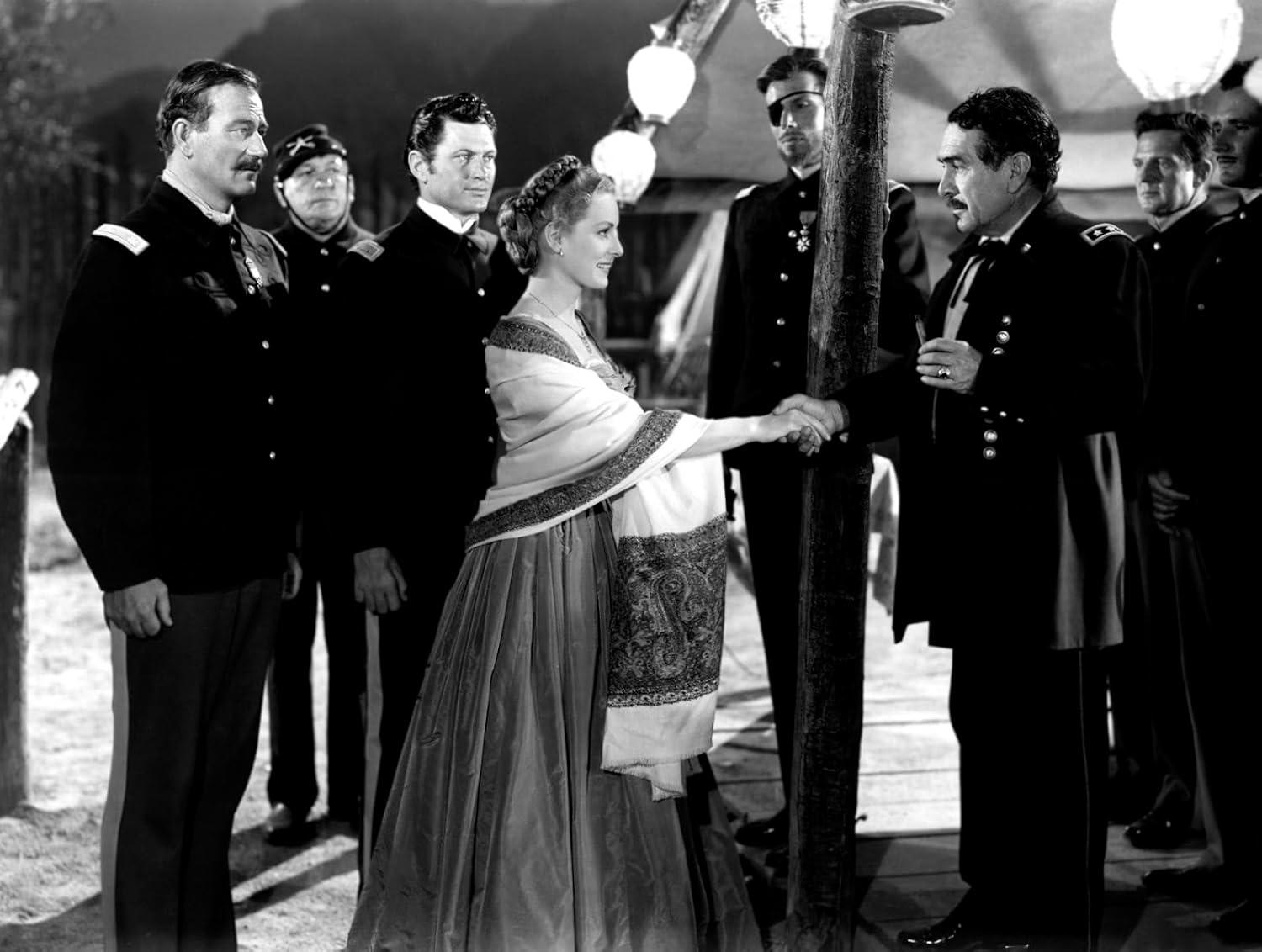 Eine Frau im Kleid schüttelt einem Mann in Uniform die Hand. Andere Männer in Uniform stehen um sie herum. Schwarz-Weiß-Bild.