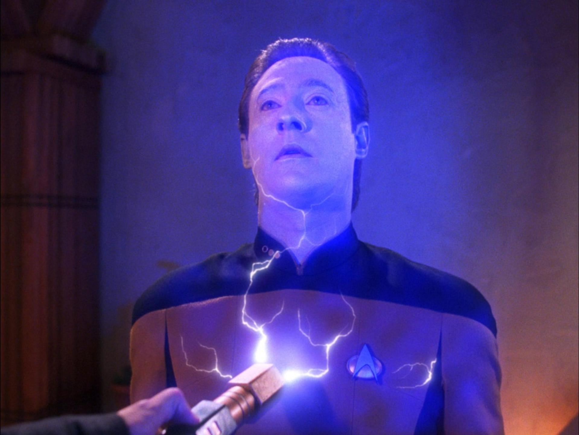 Data aus Star Trek wird von Energie getroffen. Er trägt eine Uniform mit einem Starfleet-Emblem. Der Hintergrund ist blau.