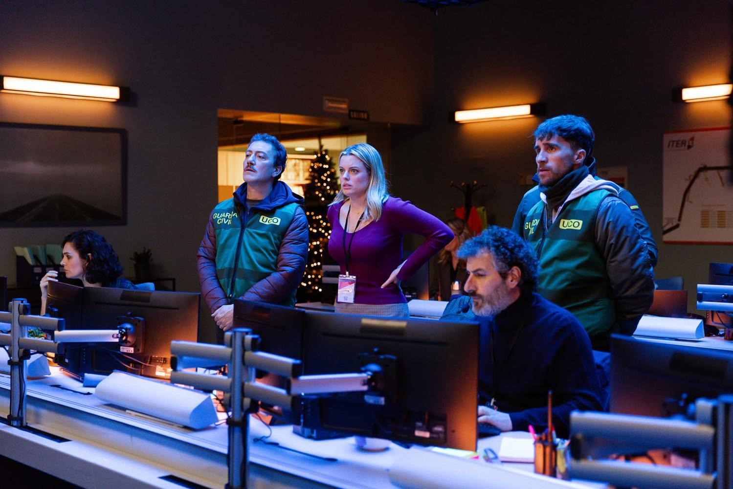 Menschen in einem Kontrollraum. Drei Männer und eine Frau blicken nach oben. Andere arbeiten an Computern. Weihnachtsbaum im Hintergrund.