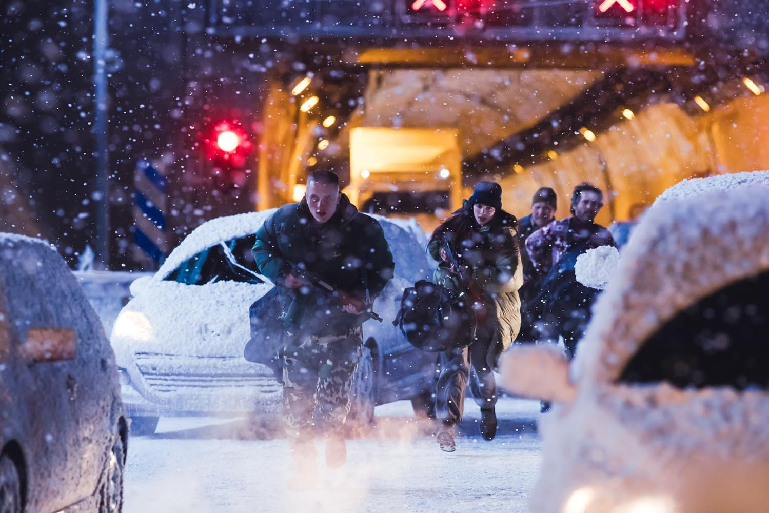 Leute rennen in einer verschneiten Szene mit Waffen. Autos sind mit Schnee bedeckt. Tunnel im Hintergrund mit Lichtern und roten Signalen.