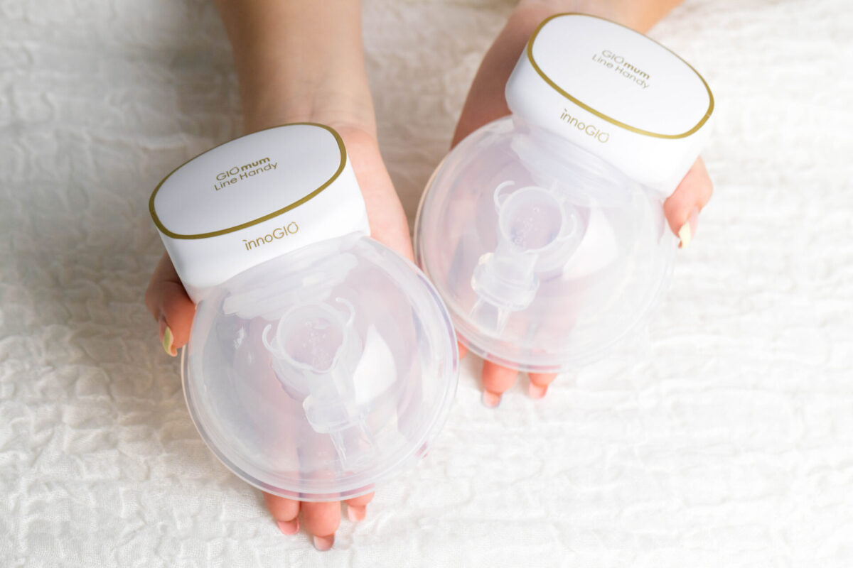 Dwie dłonie trzymają laktatory. Każdy ma biały wierzch ze złotym wykończeniem i przezroczysty, okrągły pojemnik.