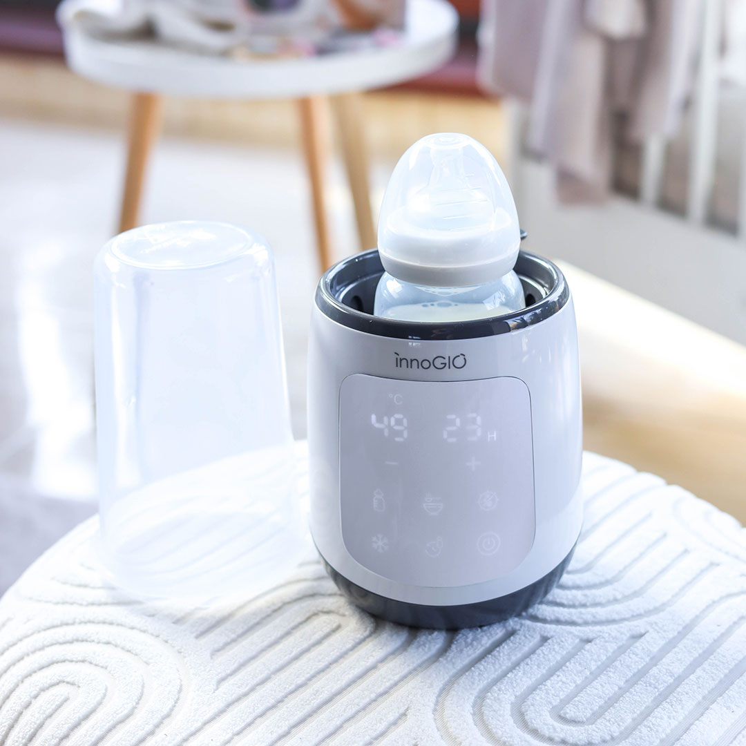 Podgrzewacz do butelek z butelką w środku. Przezroczysta osłona butelki jest po lewej stronie. Podgrzewacz ma cyfrowy wyświetlacz.