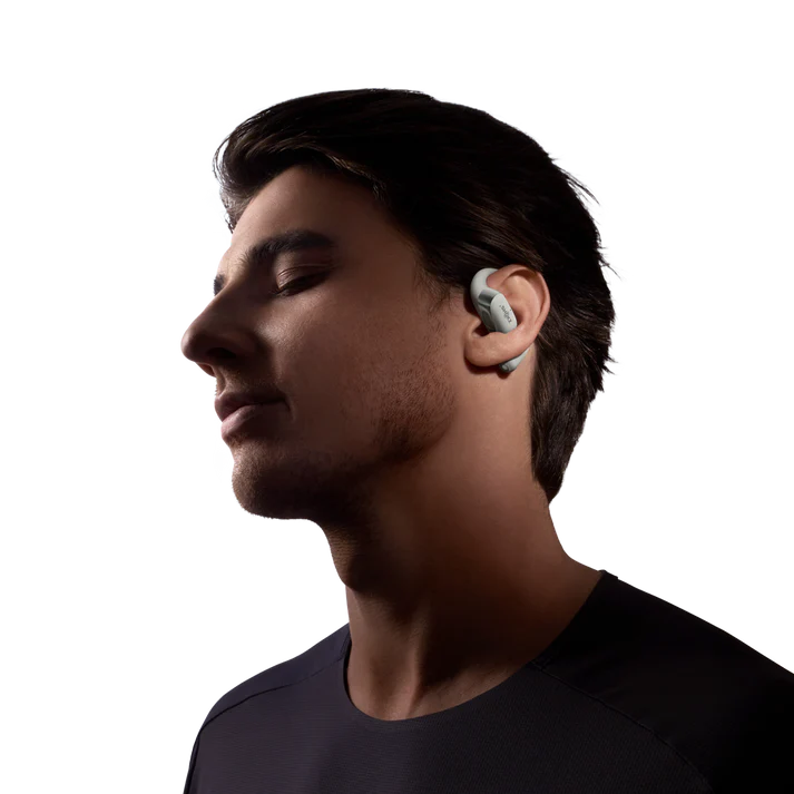 Hombre con auriculares grises, ojos cerrados, mirando a la izquierda. Camiseta oscura. Fondo negro. Auriculares blancos.