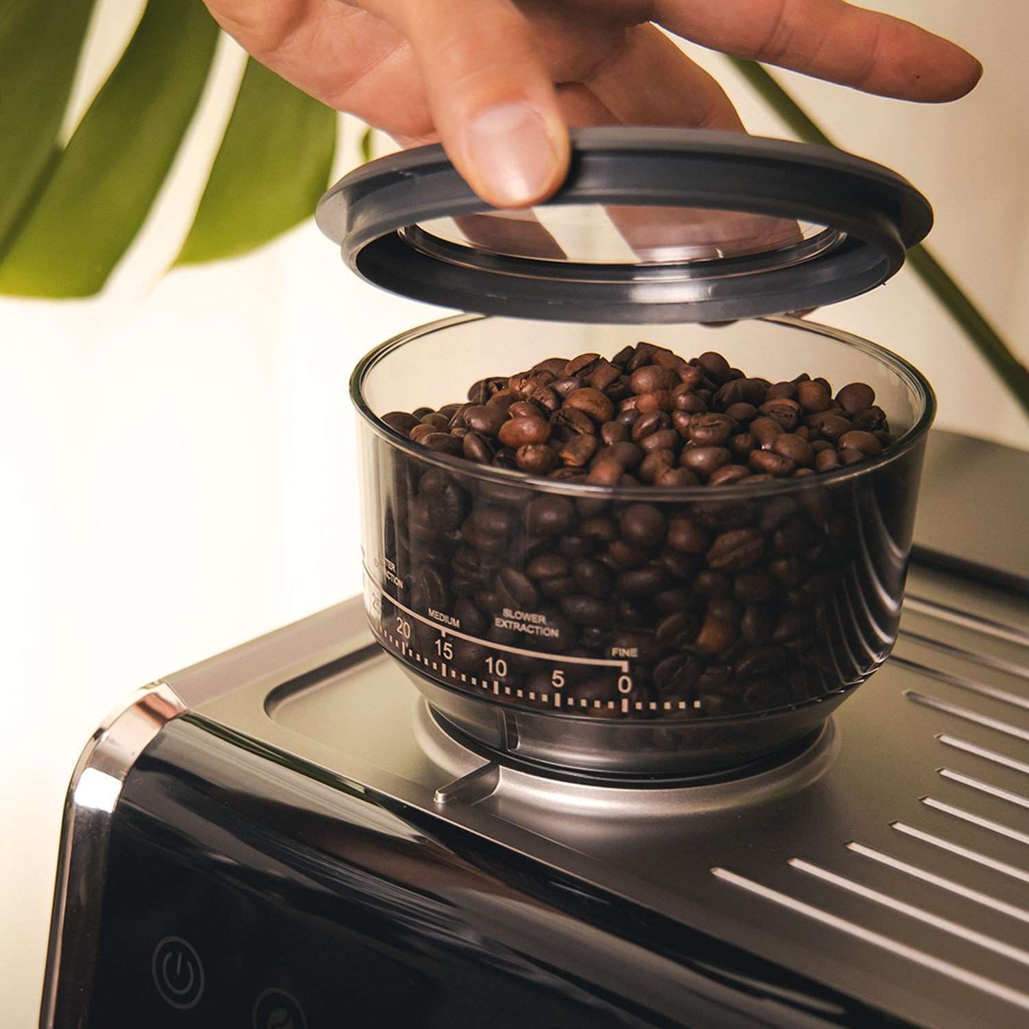 Una mano solleva il coperchio di un contenitore di vetro pieno di chicchi di caffè. Il contenitore è su una macchina per il caffè.