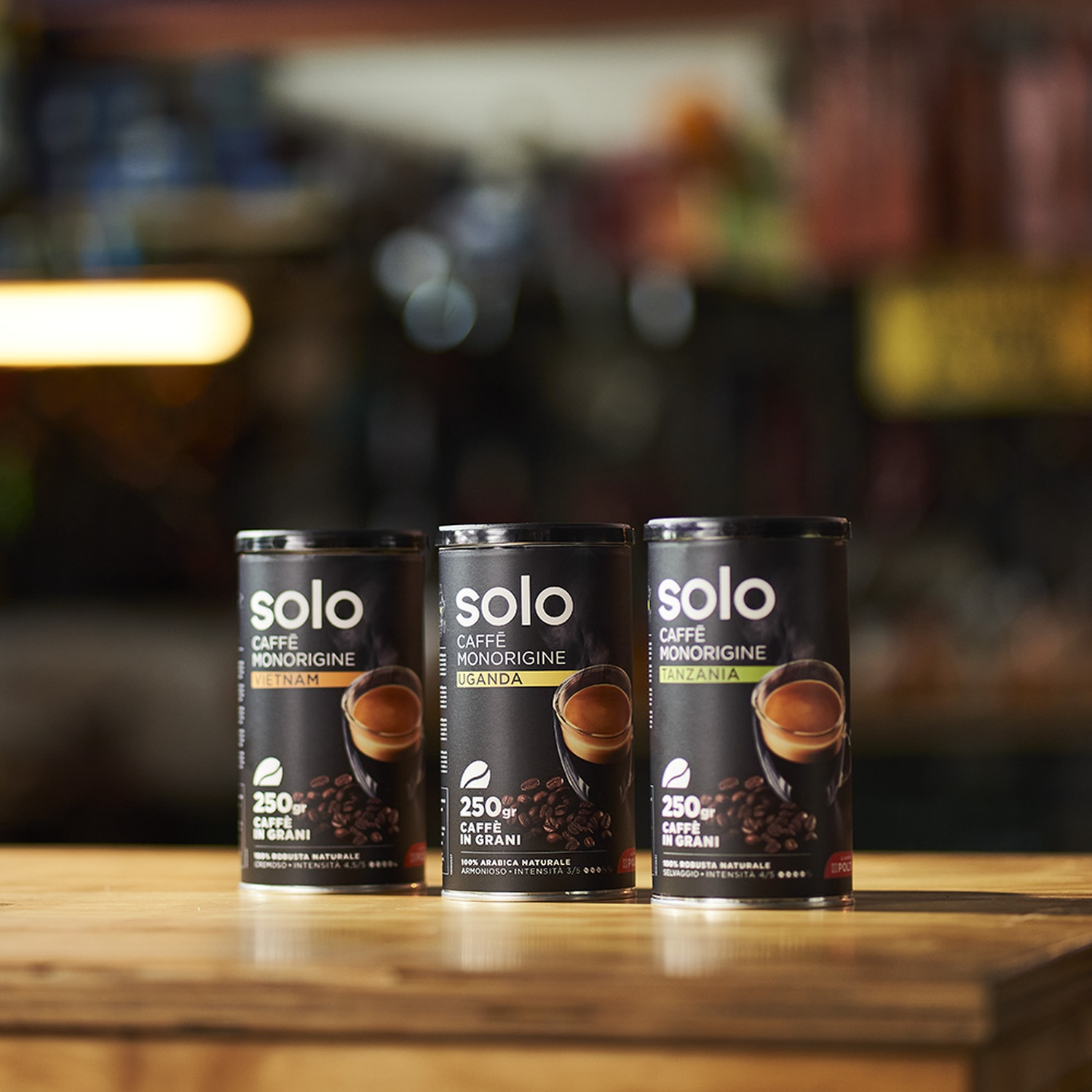 Tre lattine di caffè con il marchio Solo su una superficie di legno. Ogni lattina mostra chicchi di caffè e l'immagine di una tazza.