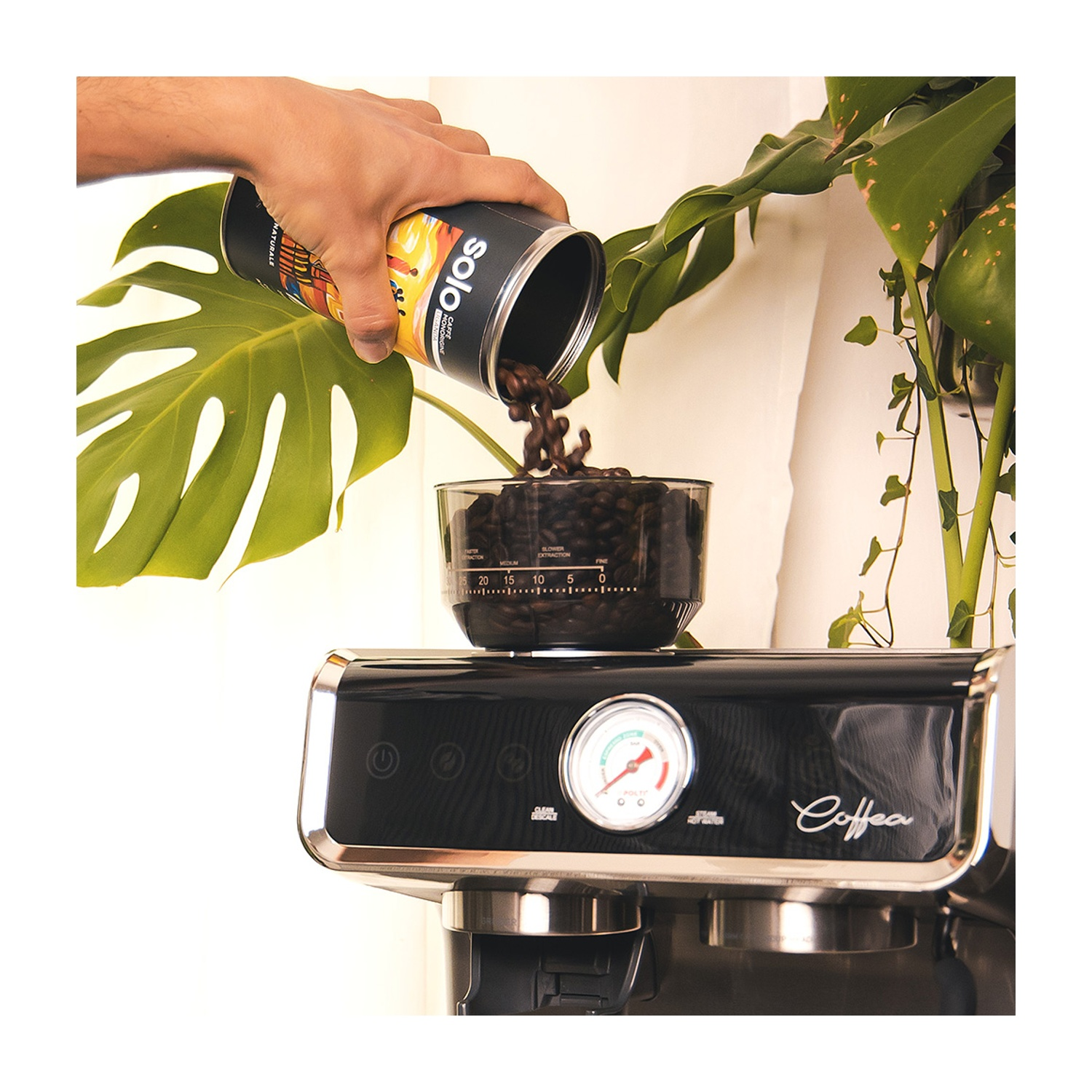 Una mano versa chicchi di caffè da una lattina Solo in un contenitore di vetro su una macchina per caffè espresso nera, con piante verdi sullo sfondo.