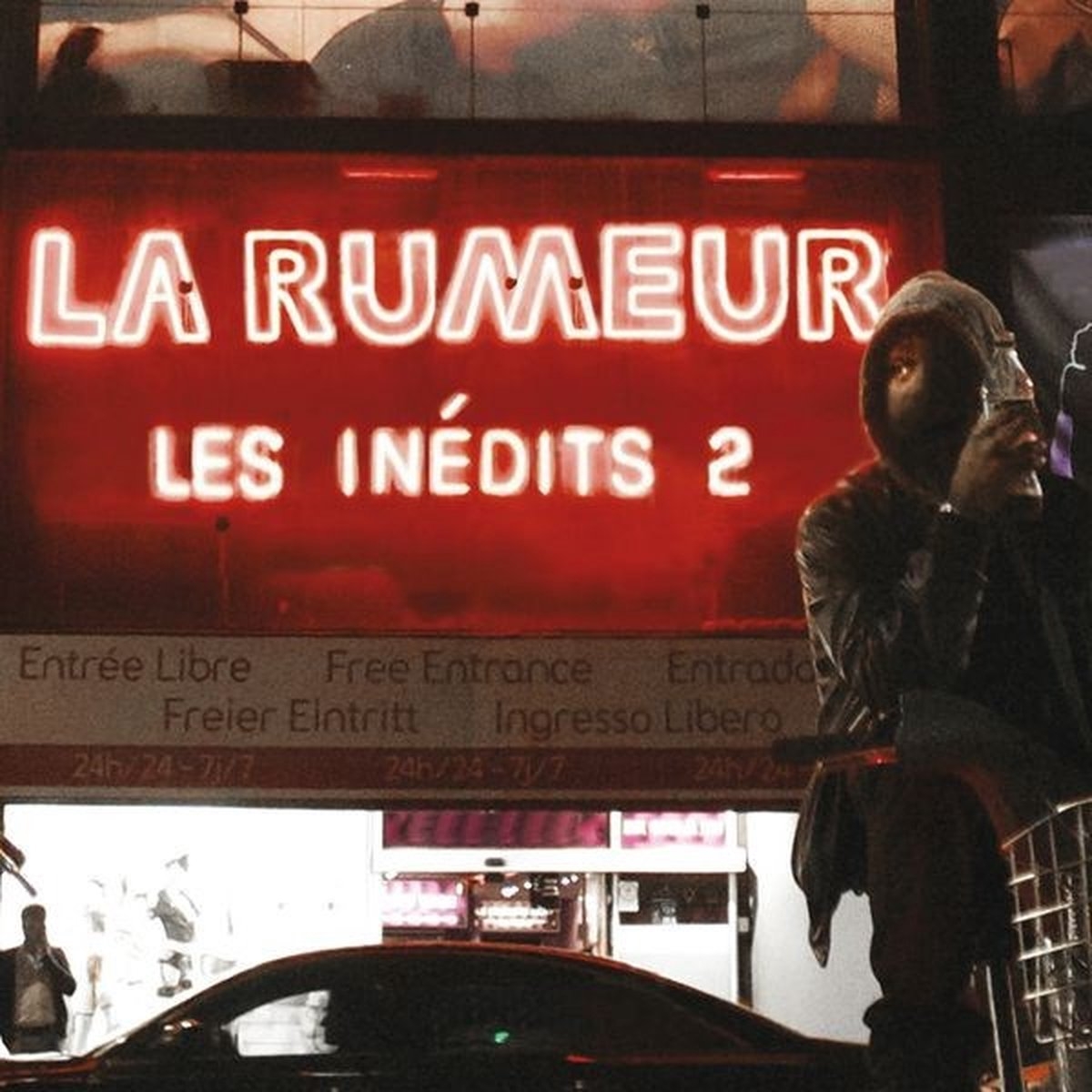 Een neonreclame leest 'LA RUMEUR LES INÉDITS 2'. Een persoon met een hoodie houdt een fles vast. Een auto staat op de voorgrond.