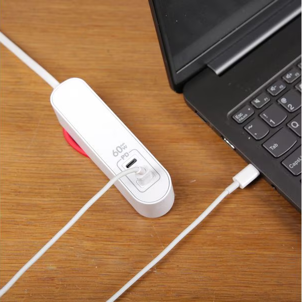Un adattatore di alimentazione bianco è collegato a un laptop tramite un cavo bianco. L'adattatore si trova su una superficie di legno.