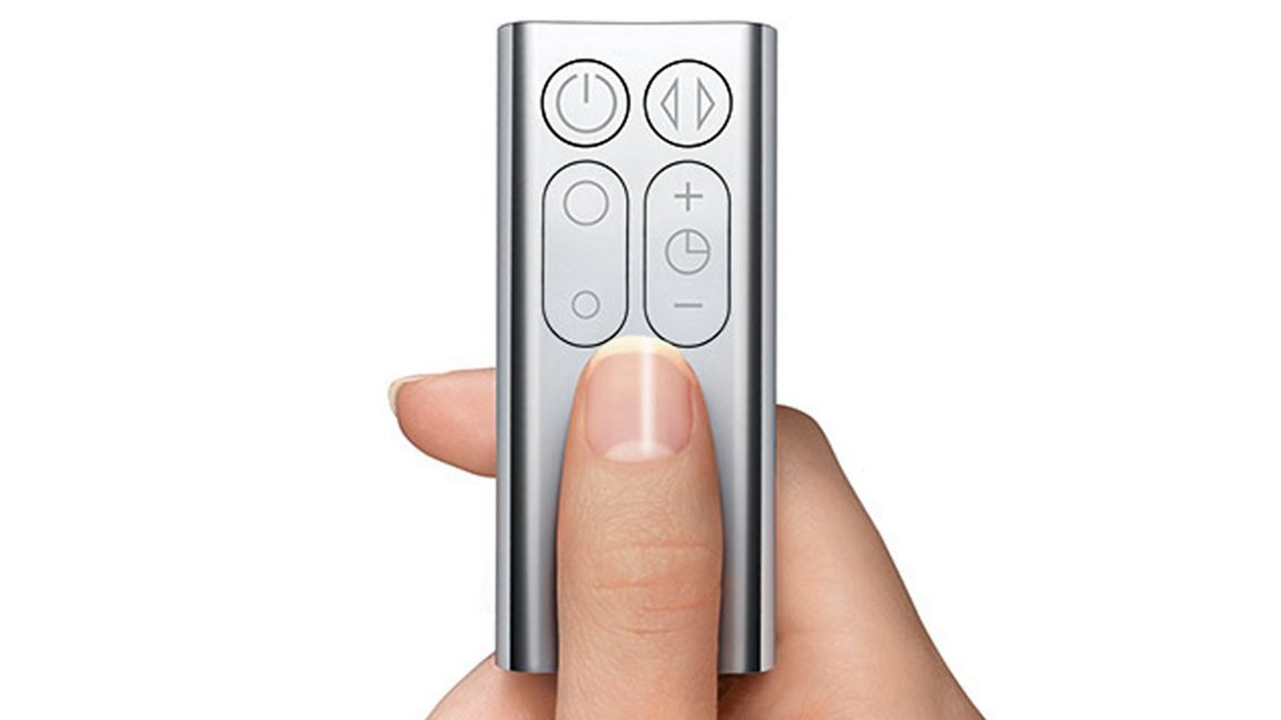 Une main tient une télécommande argentée. Un doigt appuie sur un bouton. La télécommande comporte des commandes d'alimentation, de volume et de minuterie.