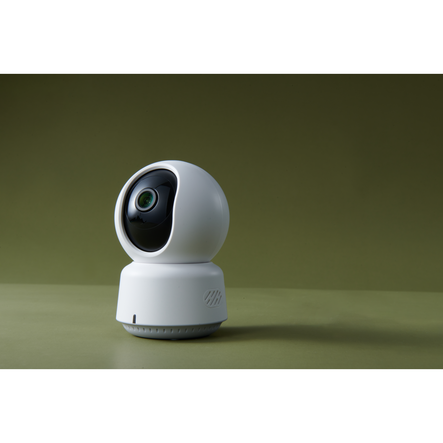 A white security camera on a green surface against a green background. The camera has a black lens.