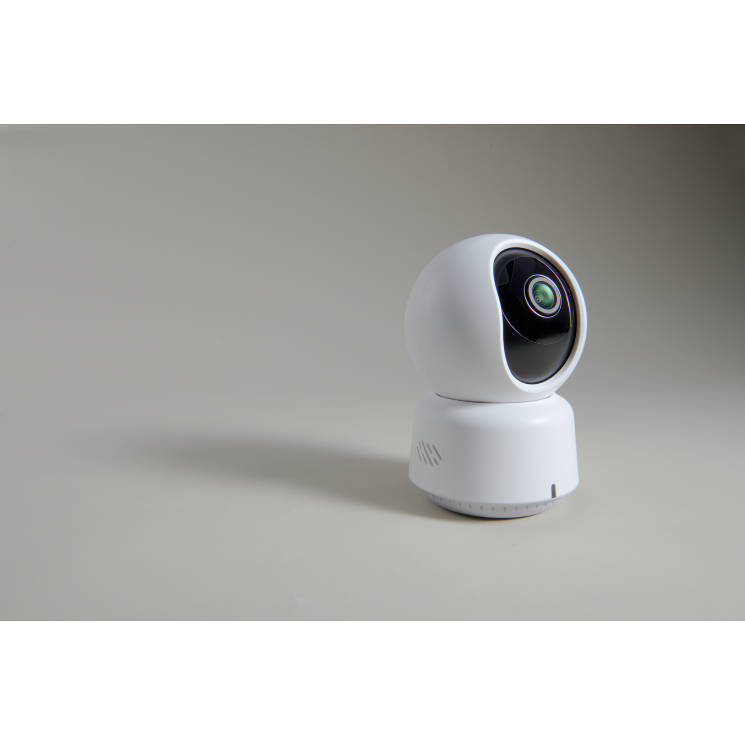 A white security camera with a black lens sits on a light gray surface. It has a round top and a cylindrical base.