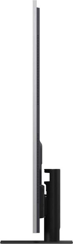 Una TV sottile e moderna è in piedi. Ha una cornice argentata, bordi neri e un supporto nero. Il profilo laterale è visibile.