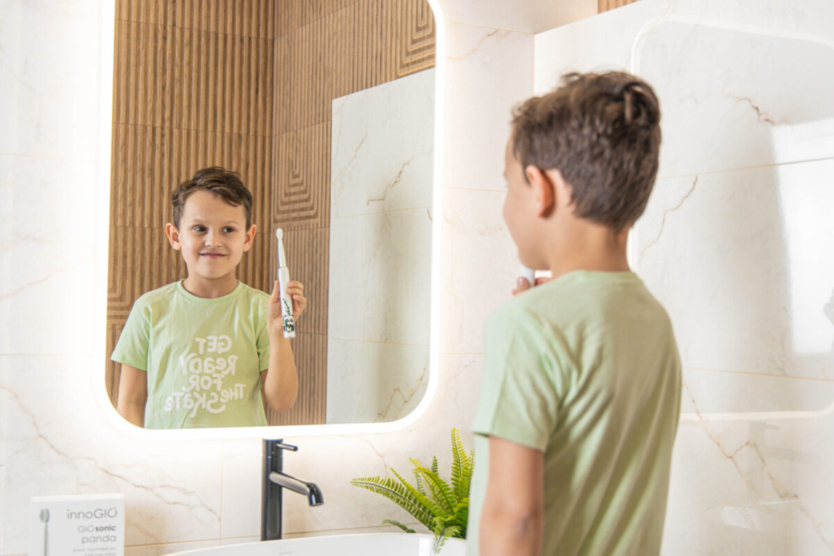 Chłopiec myje zęby w łazience. Odbija się w lustrze, trzymając szczoteczkę. Tło ma drewniane panele.