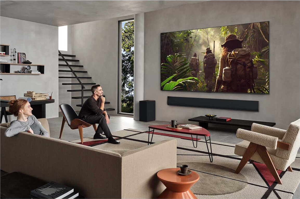 Ein Paar schaut im modernen Wohnzimmer fern. Der Fernseher zeigt eine Dszene. Es gibt moderne Möbel und ein Fenster.