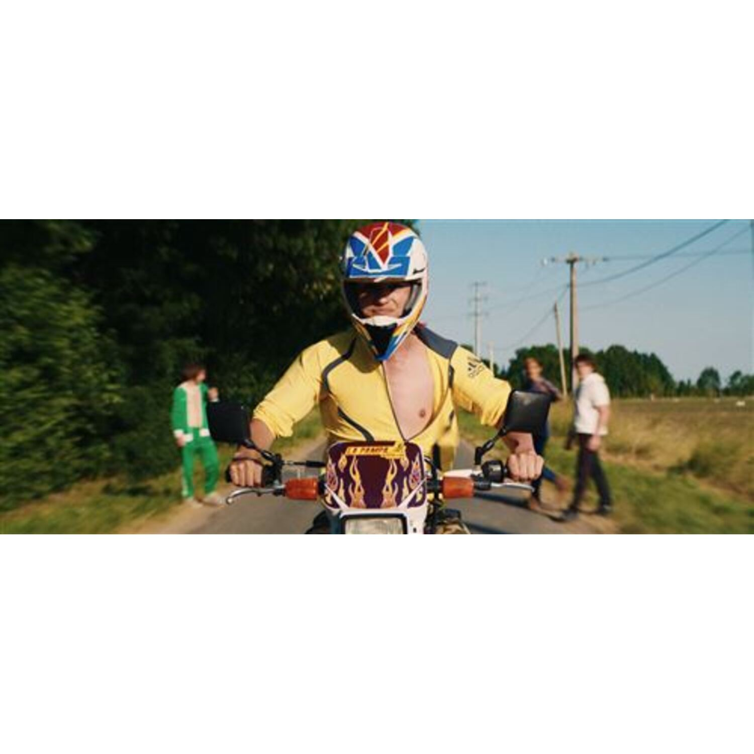 Een persoon op een motor met helm en gele jas. Twee mensen lopen langs de weg.