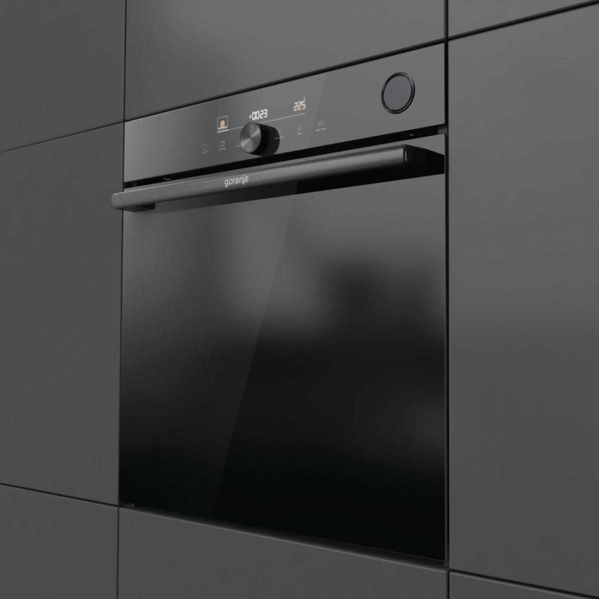 Fekete Gorenje sütő sötétszürke konyhaszekrénybe építve. A sütő ajtaja üveg. A digitális kijelző beállításokat mutat.