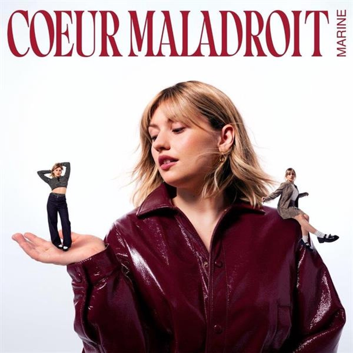 Femme en veste bordeaux avec deux figurines miniatures sur la main. Le texte en haut dit 'COEUR MALADROIT MARINE'.