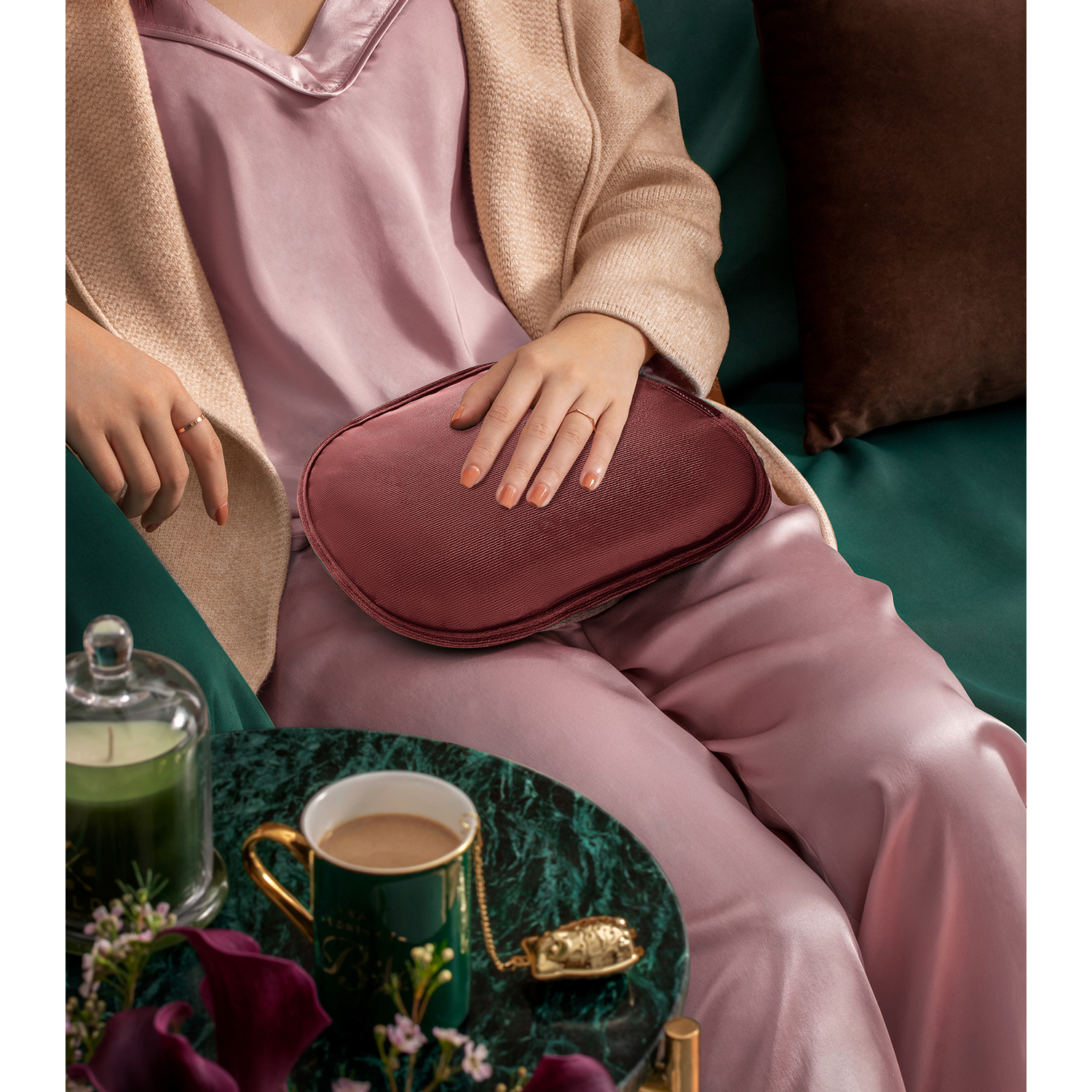 Een persoon zit met een bordeauxrood kussen. Ze draagt een roze pyjama, een beige jas. Er staat een tafel met een kop koffie voor.