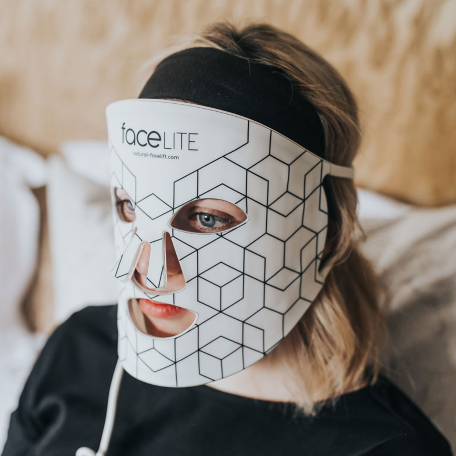 A person wearing a face mask with a geometric pattern. The mask covers the face, revealing blue eyes and red lips. A black shirt is worn.