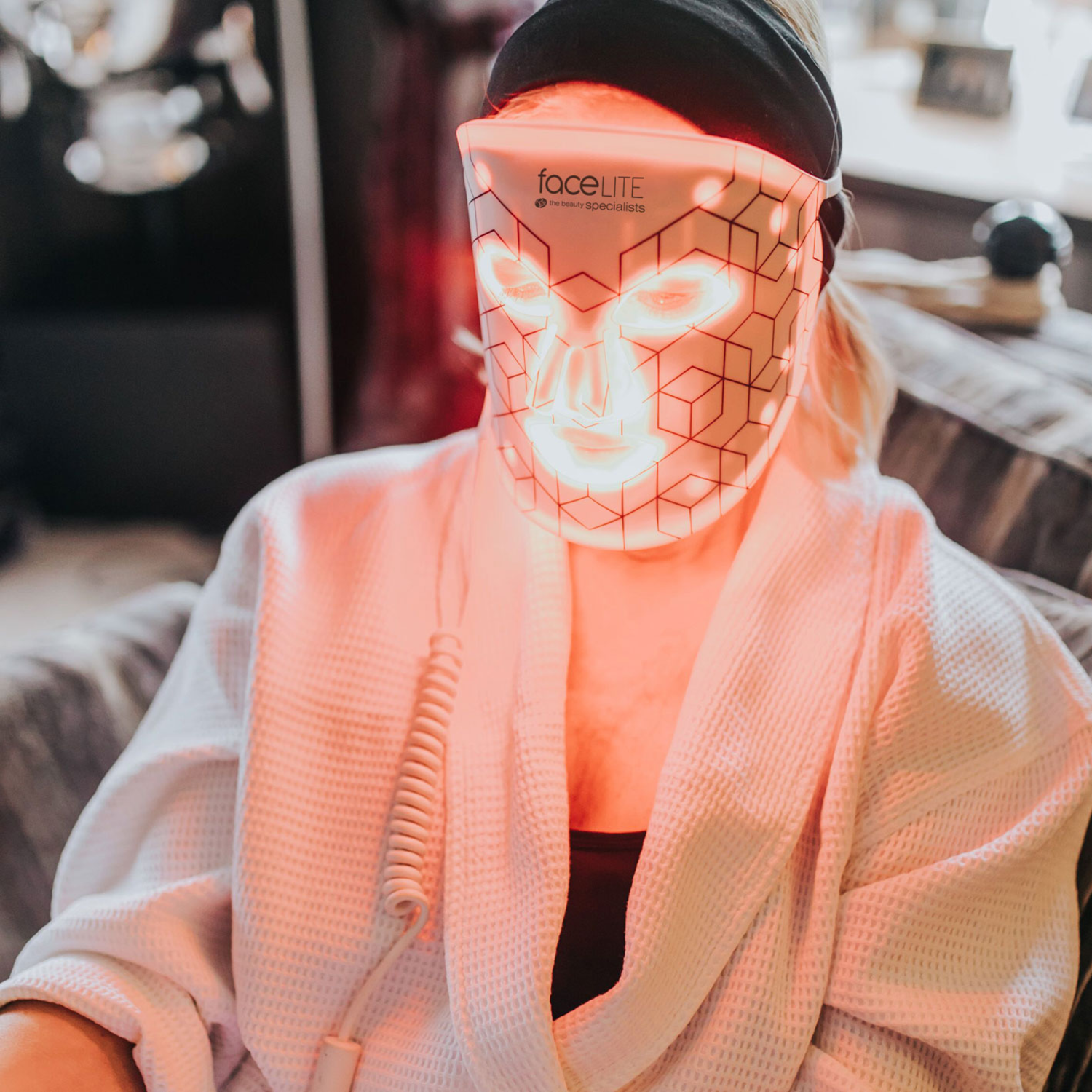 Person wearing a face light mask. They are wearing a white robe. The mask is lit up, and the room is softly lit.