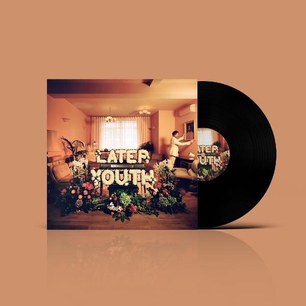 Albumcover von "Later Youth" mit Schallplatte. Es zeigt einen Raum mit Blumenbuchstaben. Ein Mann hängt ein Bild auf.