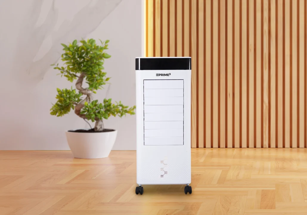 Biała chłodziarka powietrza stoi na kółkach. Z lewej strony bonsai w białej doniczce. Tło to drewniane panele.