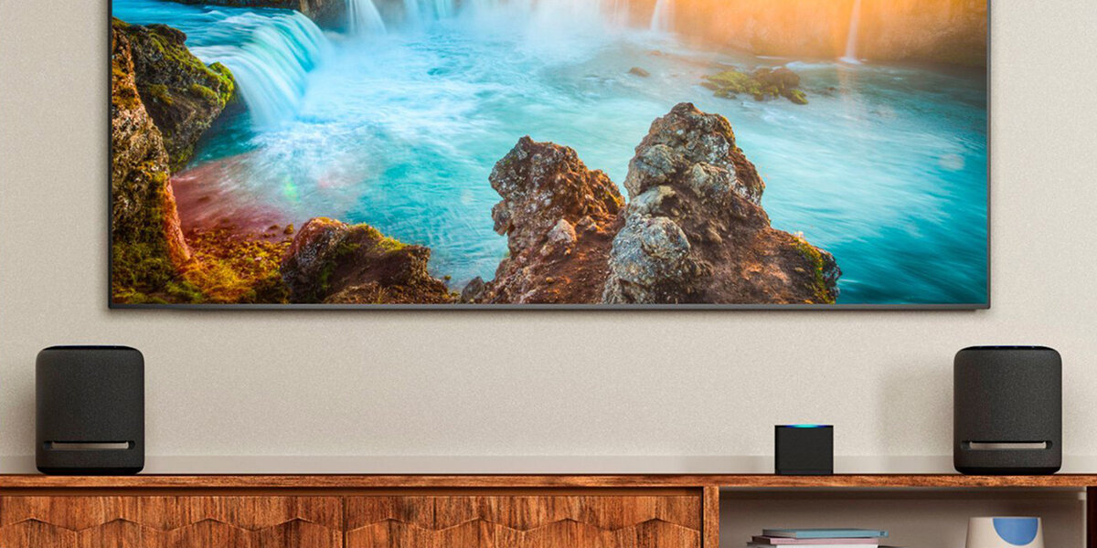 Telewizor wyświetla scenę wodospadu. Głośniki i inteligentne urządzenie znajdują się na drewnianej szafce pod telewizorem.