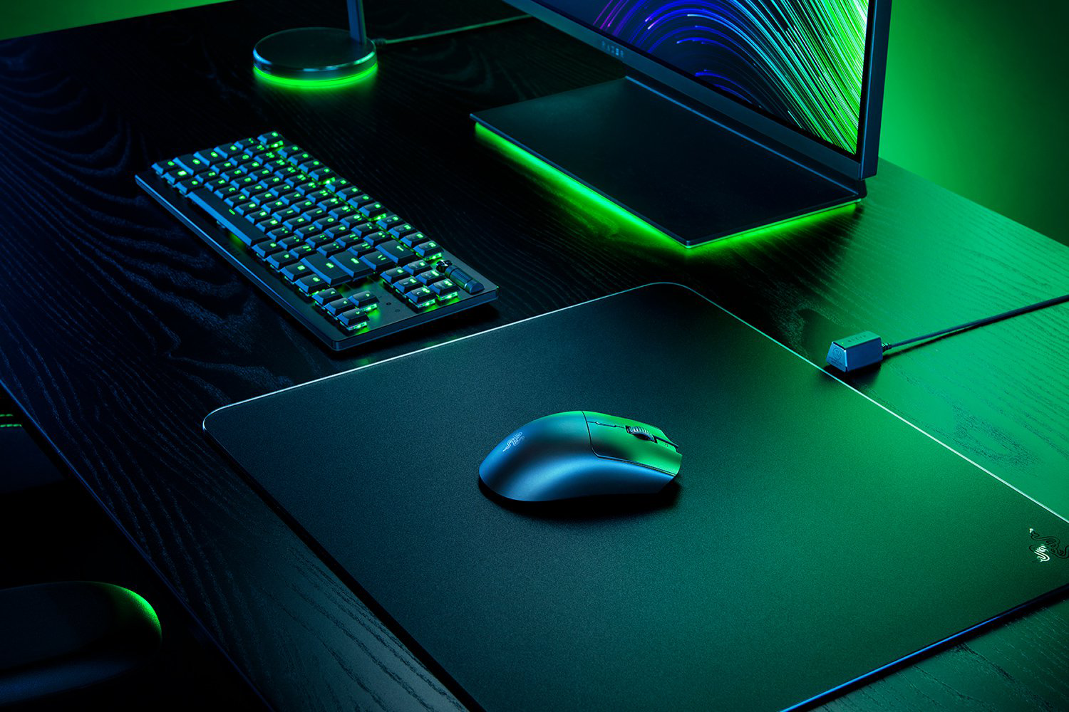 Egy gamer beállítás billentyűzettel, egérrel és monitorral egy asztalon. A jelenetet zöld és kék fények világítják meg.