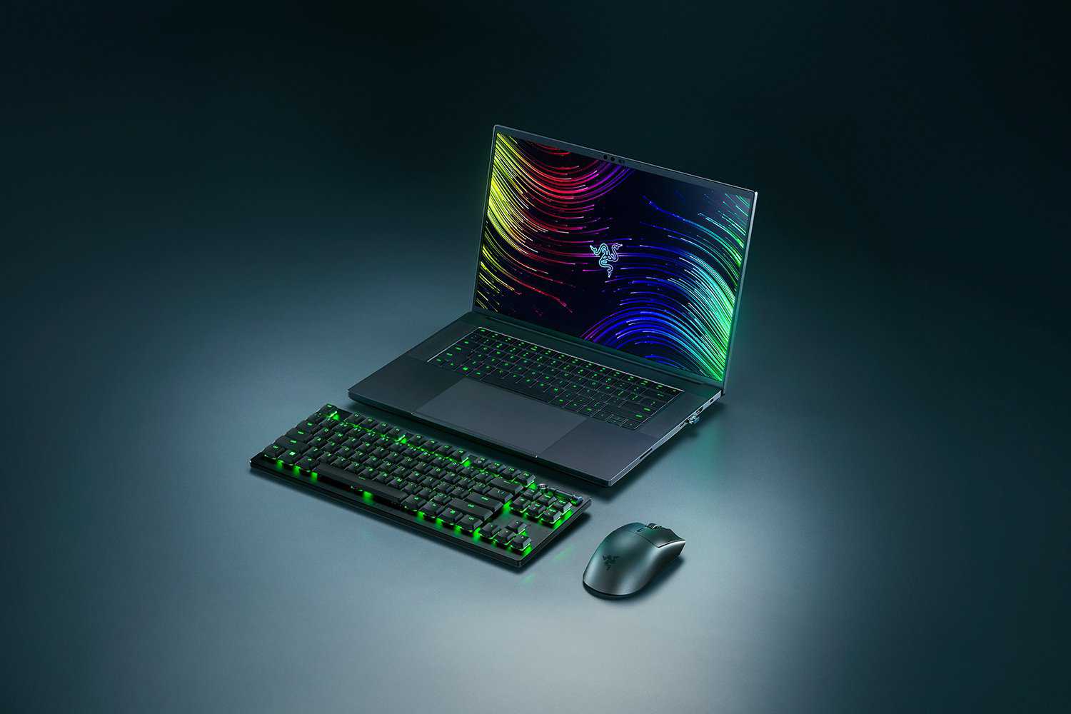 Egy fekete gamer laptop, billentyűzet és egér. A laptop képernyőjén színes vonalak láthatók. Zöld fények világítják meg a billentyűzetet.