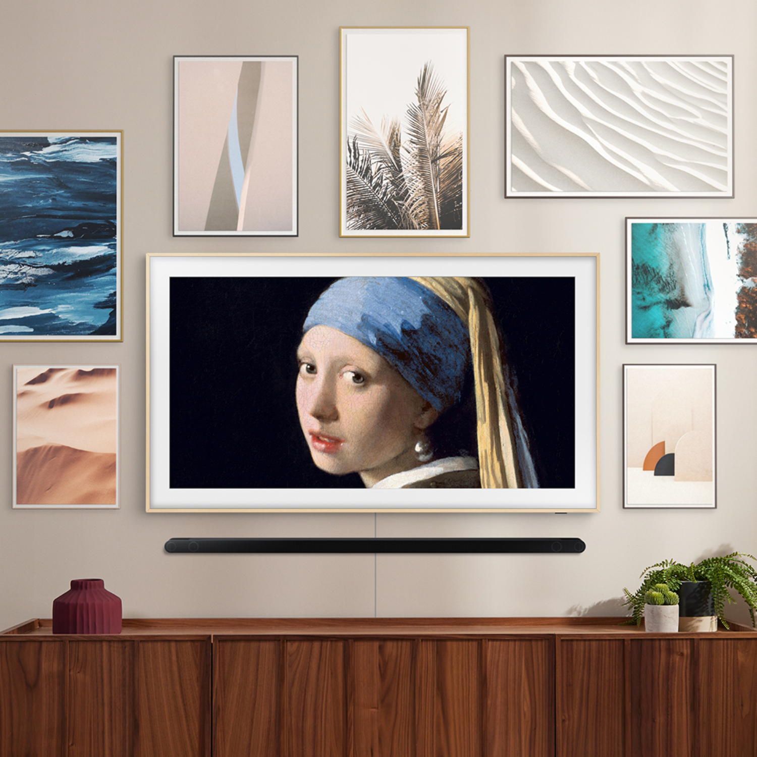 A wall with framed art and a TV displaying a woman with a blue headscarf. A soundbar sits below the TV on a wood cabinet.