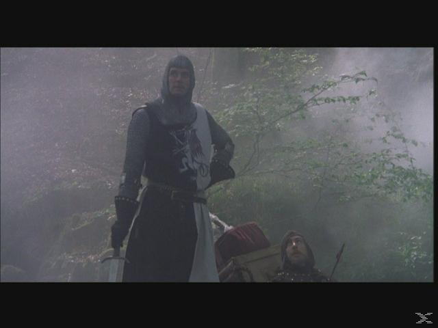 Ein Ritter in Rüstung steht in einem Wald. Eine weitere Person ist im Hintergrund. Der Ritter hält ein Schwert. Die Szene ist neblig.