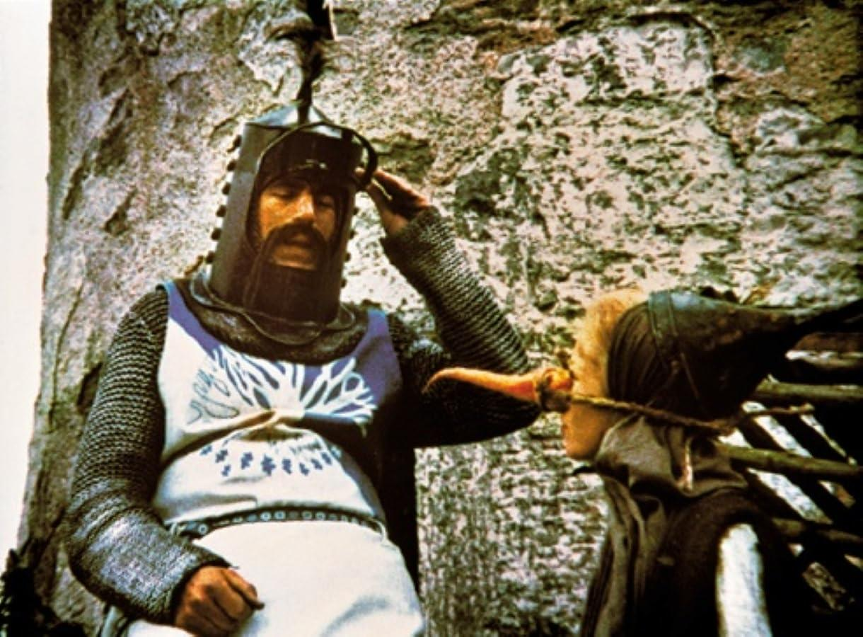 Ein Ritter mit Helm und Kettenhemd salutiert. Eine Person wird mit einem Holzstab geknebelt.