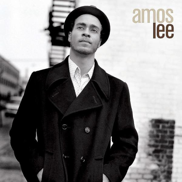 Mann in schwarzem Mantel und Hut, der nach oben blickt. Im Hintergrund eine Backsteinmauer und der Name "Amos Lee".