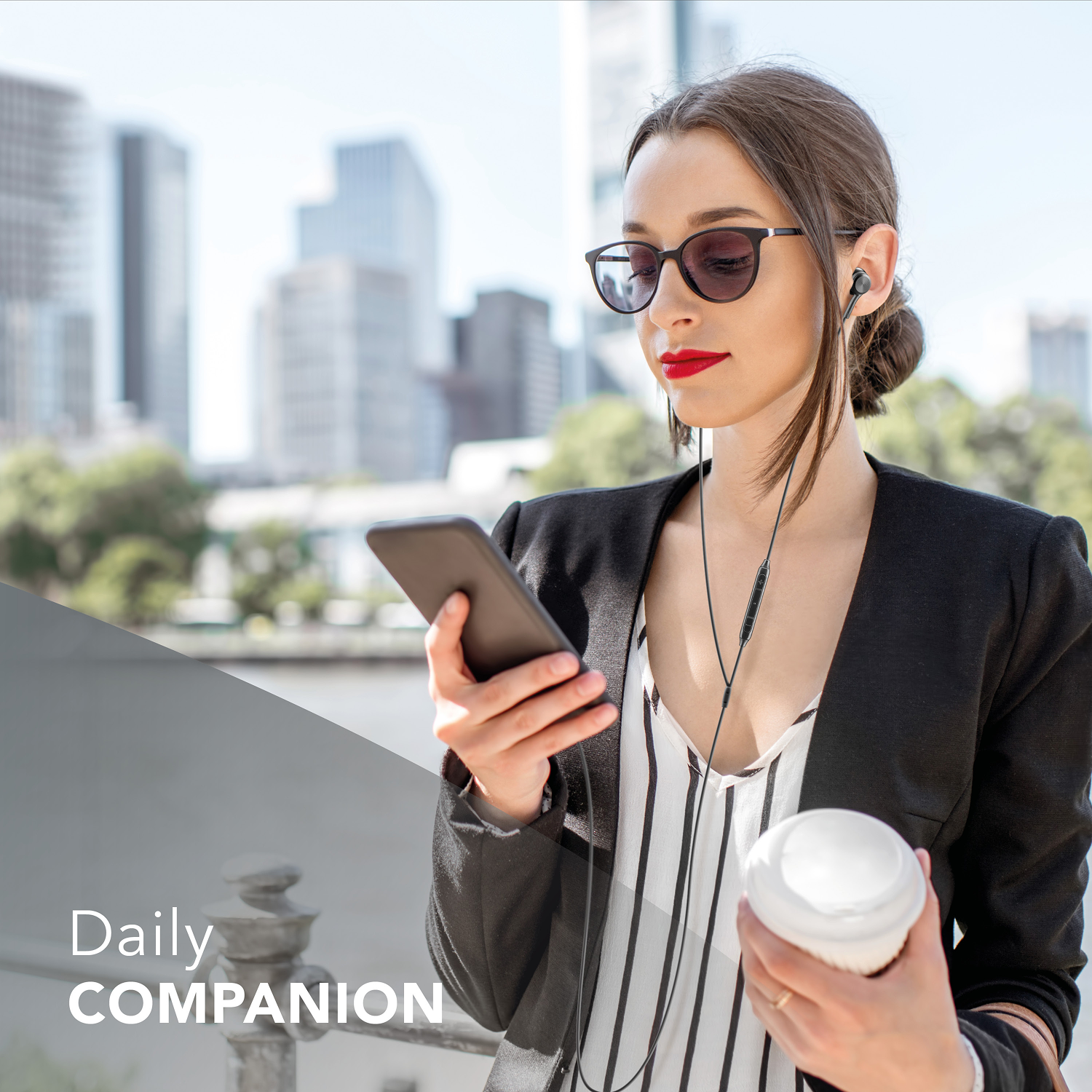 Mujer con gafas de sol, sosteniendo un teléfono y una taza de café, con auriculares, con edificios de la ciudad al fondo.