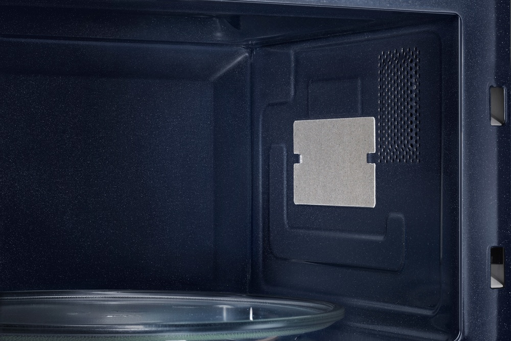 Dentro de un microondas azul oscuro. Una placa de vidrio en la parte inferior. Una placa de metal rectangular y una ventilación a la derecha.