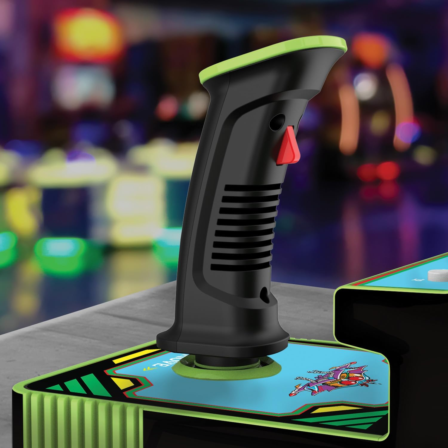 Primer plano de un joystick negro con parte superior y base verdes. Hay un botón rojo en el lateral. El joystick está sobre una superficie azul.