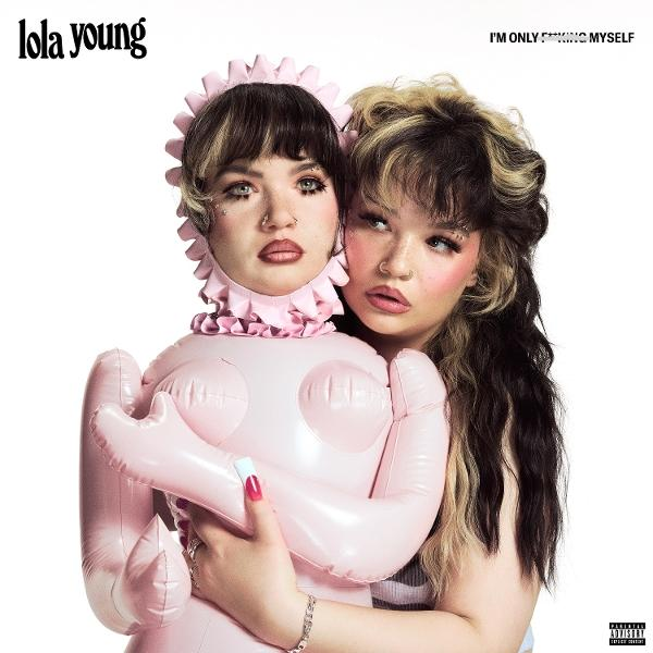 Twee jonge vrouwen. Eén houdt een roze opblaaspop vast. De andere omhelst haar. Tekst: Lola Young, I'M ONLY F***ING MYSELF.