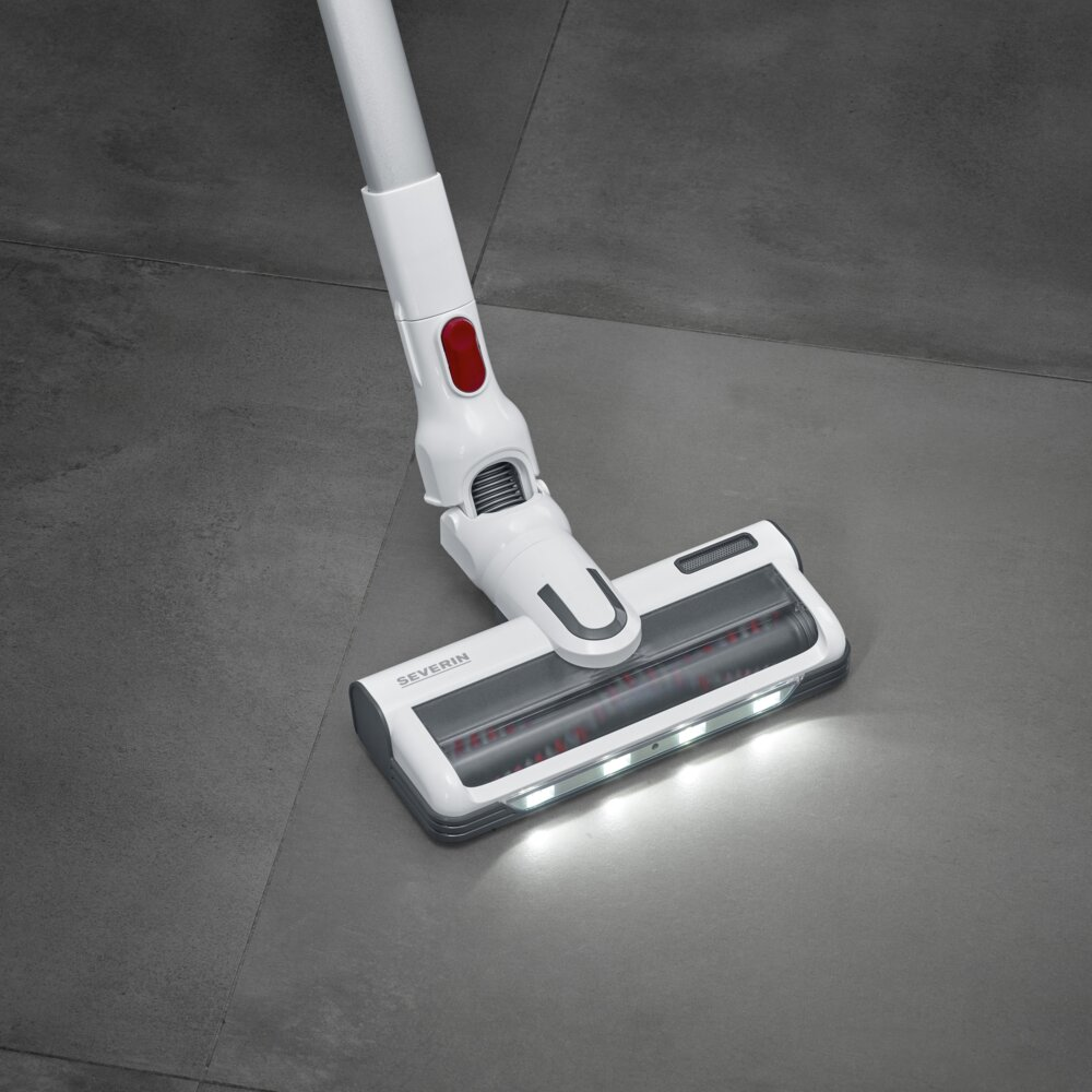 Biały i szary odkurzacz z czerwonym przyciskiem, spoczywający na szarej podłodze z płytek. Głowica odkurzacza ma światła.