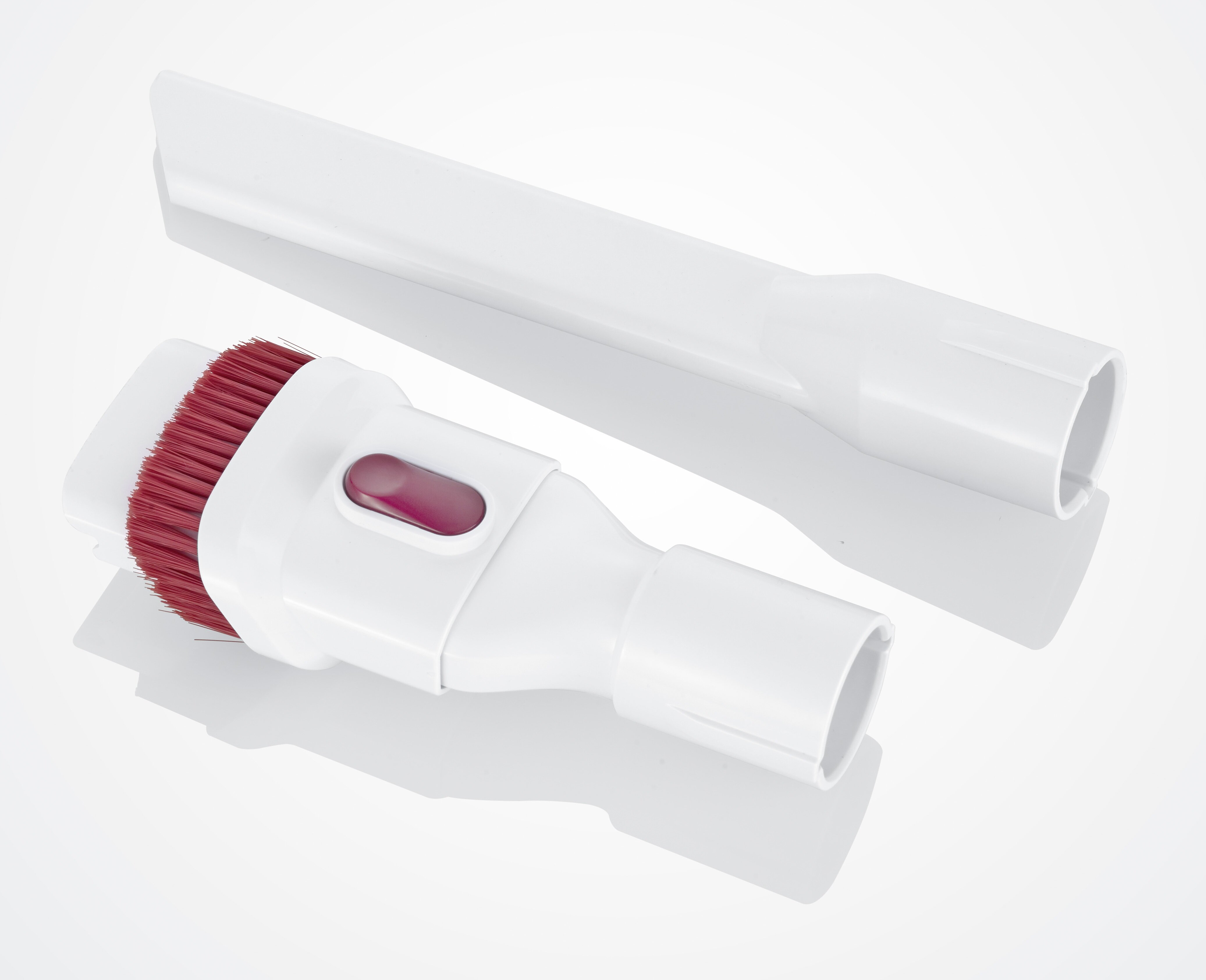 Dwie białe nasadki do odkurzacza. Jedna ma czerwone włosie, druga to ssawka szczelinowa. Obie na białej powierzchni.