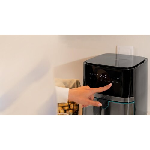 Ręka dotyka wyświetlacza czarnej frytkownicy ustawionej na 200 stopni. Frytkownica stoi na blacie w kuchni.