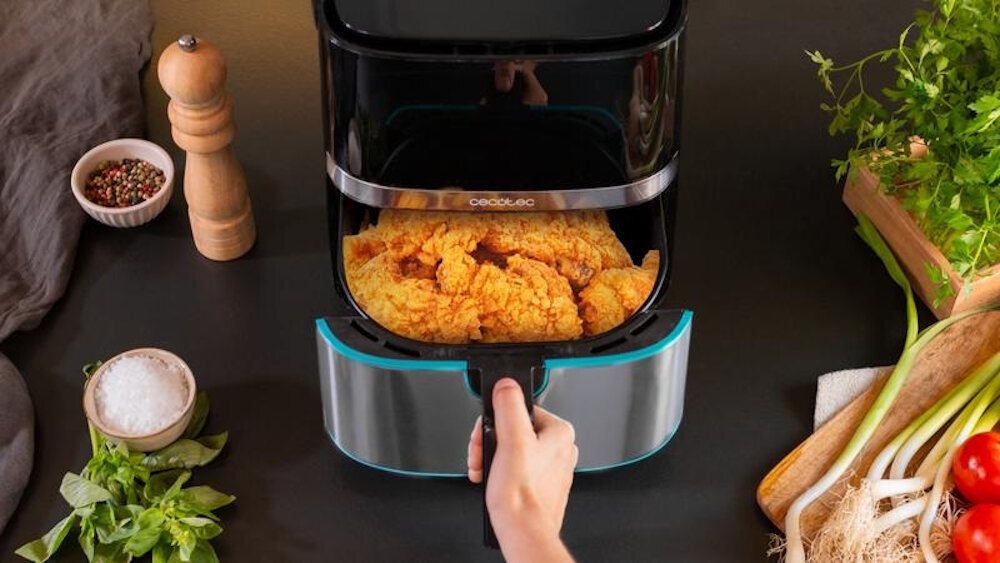 Frytkownica powietrzna z smażonym jedzeniem. Na stole sól, zioła, pieprz i warzywa.