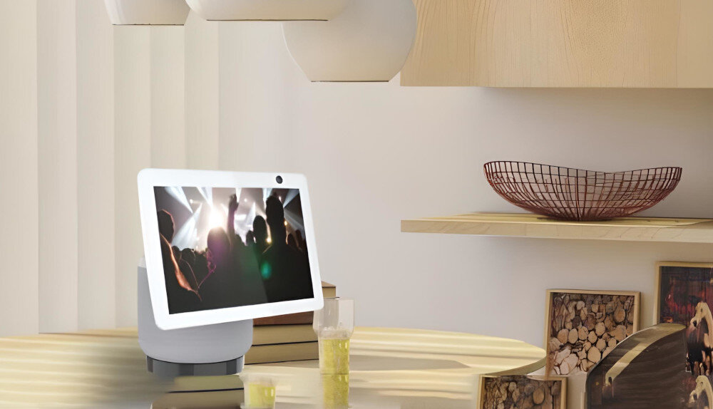 Inteligentny wyświetlacz pokazuje nagrania z koncertu. Na stole, ze szklankami i dekoracjami. Tło z półkami i pasiastej ścianie.