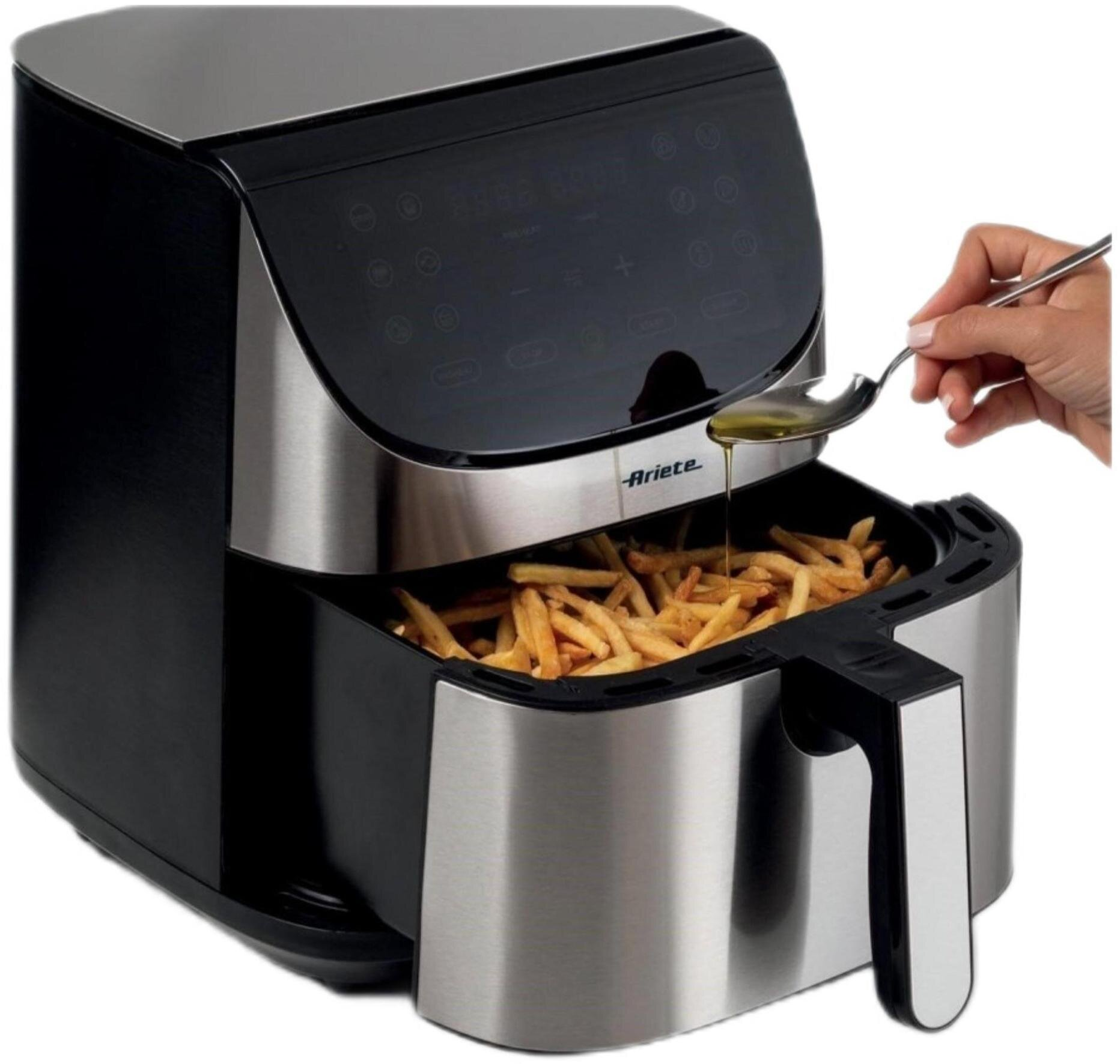 Frytownica powietrzna z frytkami w środku. Ręka wlewa olej z łyżki na frytki.